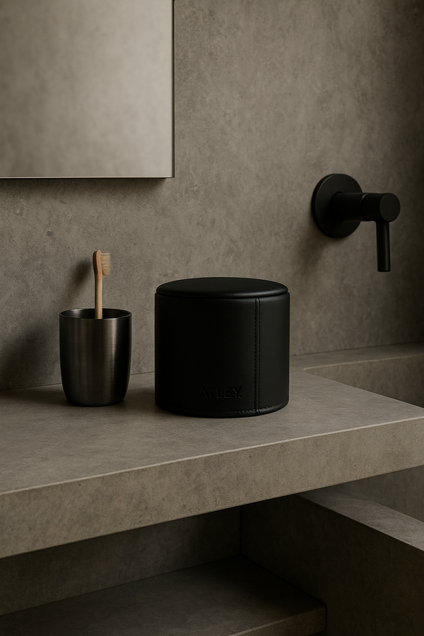 Black leather toilet roll cover. Black leather container and toothbrush holder on a bathroom counter with a neutral wall background