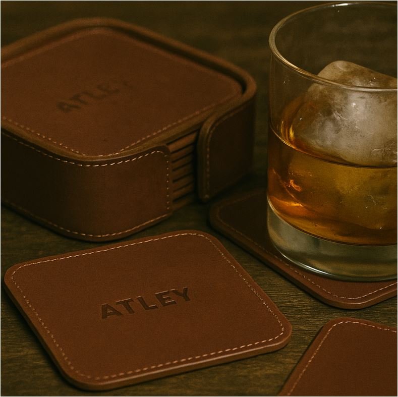 Brown leather coasters with 'ATLEY' branding next to a glass of whiskey on a wooden surface.