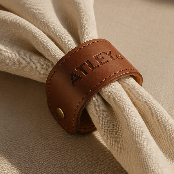 Brown leather napkin ring with 'ATLEY' branding on a beige fabric background