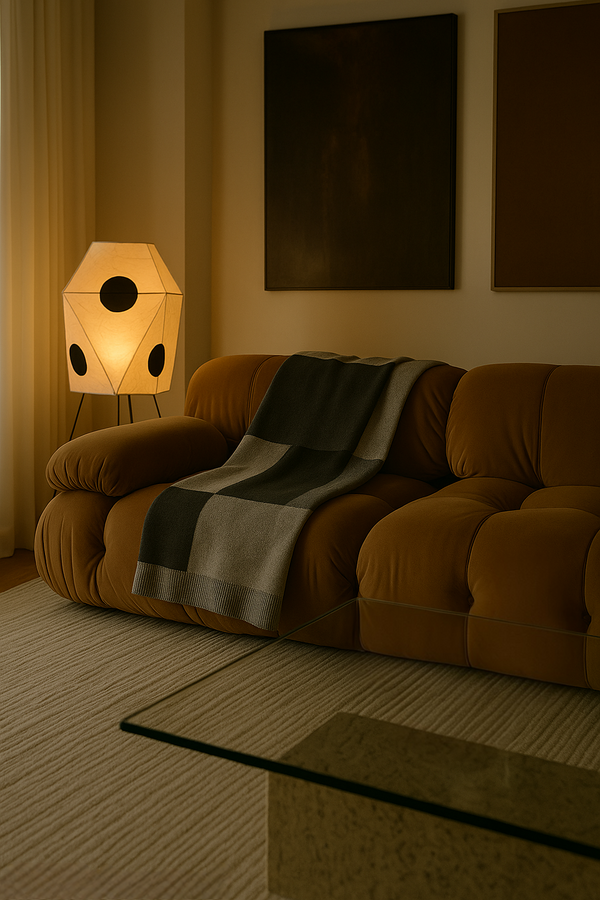 Cozy living room with brown sofa, lamp, and framed pictures on a dimly lit evening. Architectural Digest